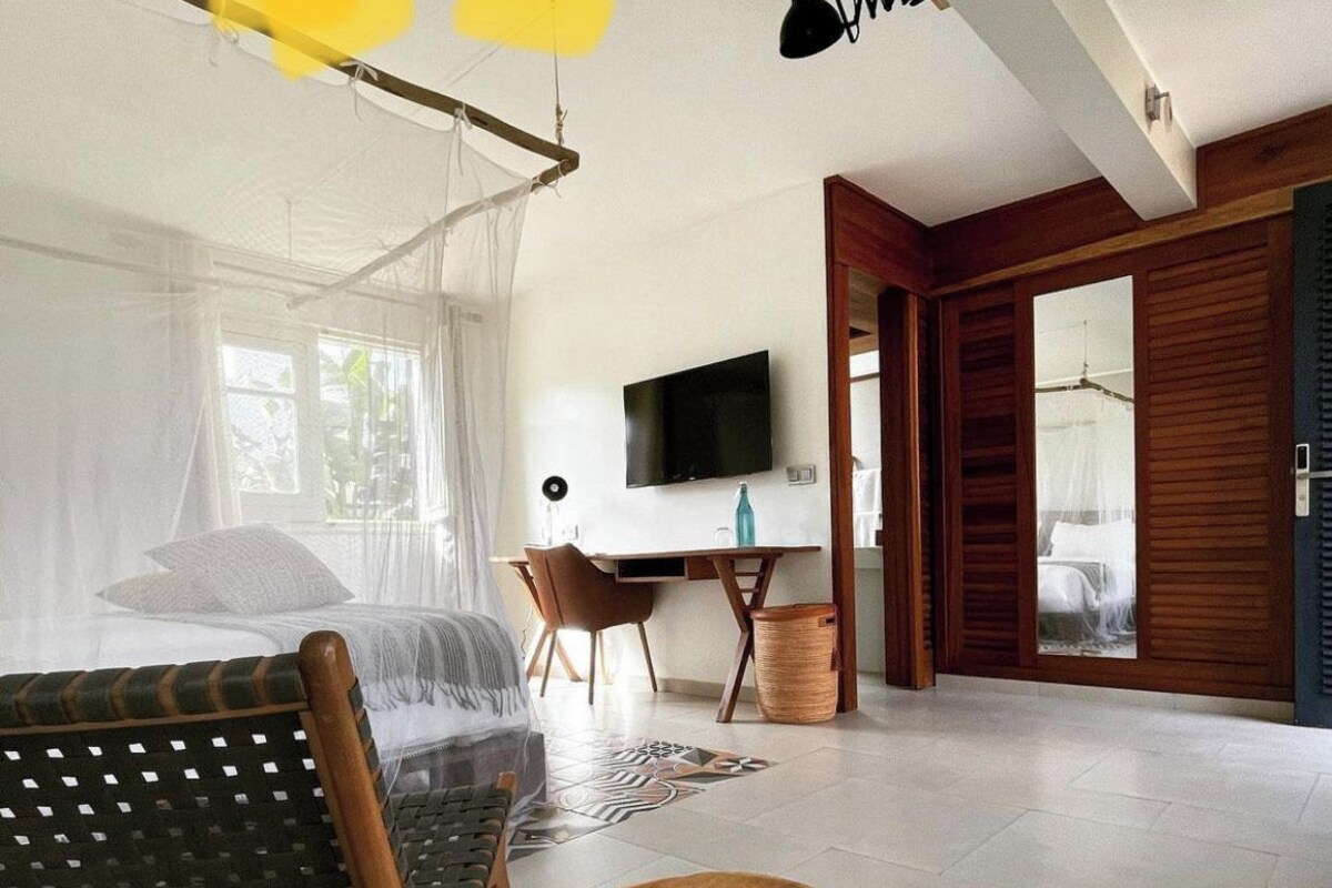 Ein modernes Schlafzimmer mit einem Bett, einem Schreibtisch, einem Fernseher und einem Korbstuhl.