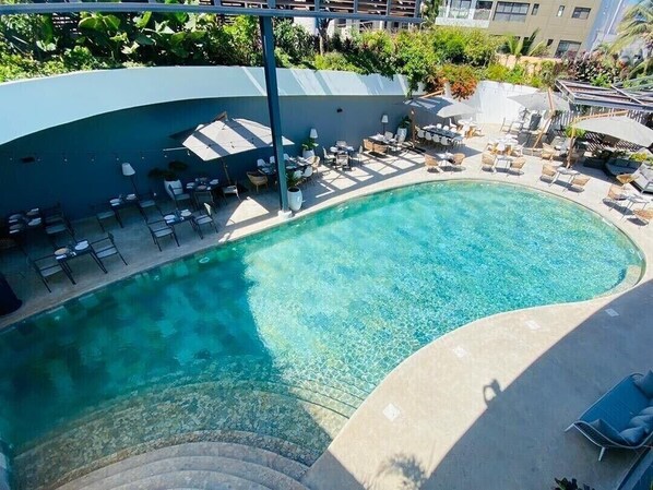 A swimming pool with lounge chairs and tables, surrounded by a curved building structure. - Hôtel Boma (Dakar)