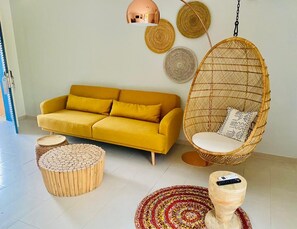 A yellow sofa, a hanging chair, and a round wooden table in a room with a tiled floor. - Hôtel Boma (Dakar)