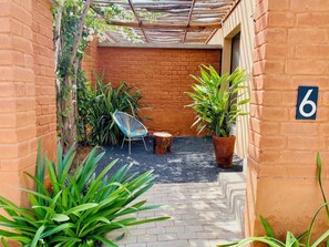 A brick-walled courtyard with a wooden pergola, a chair, potted plants, and a number '6' sign. - Hôtel Boma (Dakar)