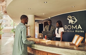 A reception desk at BOMA Lifestyle Hotel with a modern design, a laptop, a fan, and framed certificates. - Hôtel Boma (Dakar)
