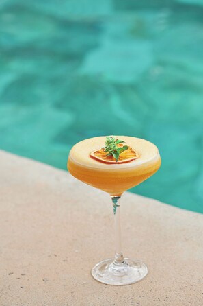 A cocktail in a martini glass with a garnish, placed on a concrete surface near a pool. - Hôtel Boma (Dakar)