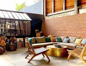 A cozy outdoor seating area with a brick wall, a round coffee table, and wicker furniture. - Hôtel Boma (Dakar)