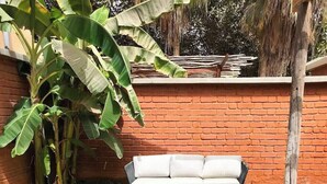 A swimming pool with a person swimming, a brick wall, a white sofa, and banana plants. - Hôtel Boma (Dakar)