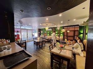 A restaurant with a modern interior, featuring a curved ceiling, green wall accents, and a variety of seating options including tables and booths. - Nancy Paradise Hotel (Haridwar)