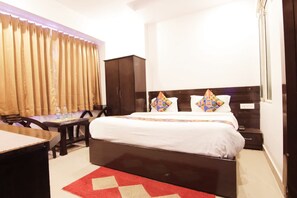 A hotel room with a bed, a desk, a wardrobe, and a red rug. - Nancy Paradise Hotel (Haridwar)