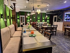 A restaurant with green wall decor, multiple dining tables, and hanging pendant lights. - Nancy Paradise Hotel (Haridwar)