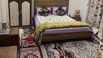 Quarto com cama de madeira, mesa de cabeceira, guarda-roupa, tapete estampado e ventoinha no teto.