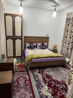 Un dormitorio con cama de madera, mesita de noche, armario, alfombra estampada y ventilador de techo.