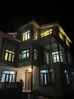 Un edificio de varios pisos con ventanas y balcones iluminados, que presenta una entrada central con puerta y un pequeño porche.