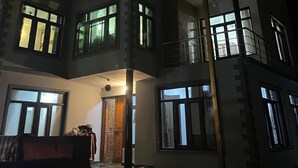 A multi-story building with illuminated windows and balconies, featuring a central entrance with a door and a small porch area. - Al Mubeen (Srinagar)