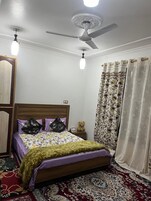 Un dormitorio con cama de madera, ropa de cama estampada, ventilador de techo y cortinas decorativas.