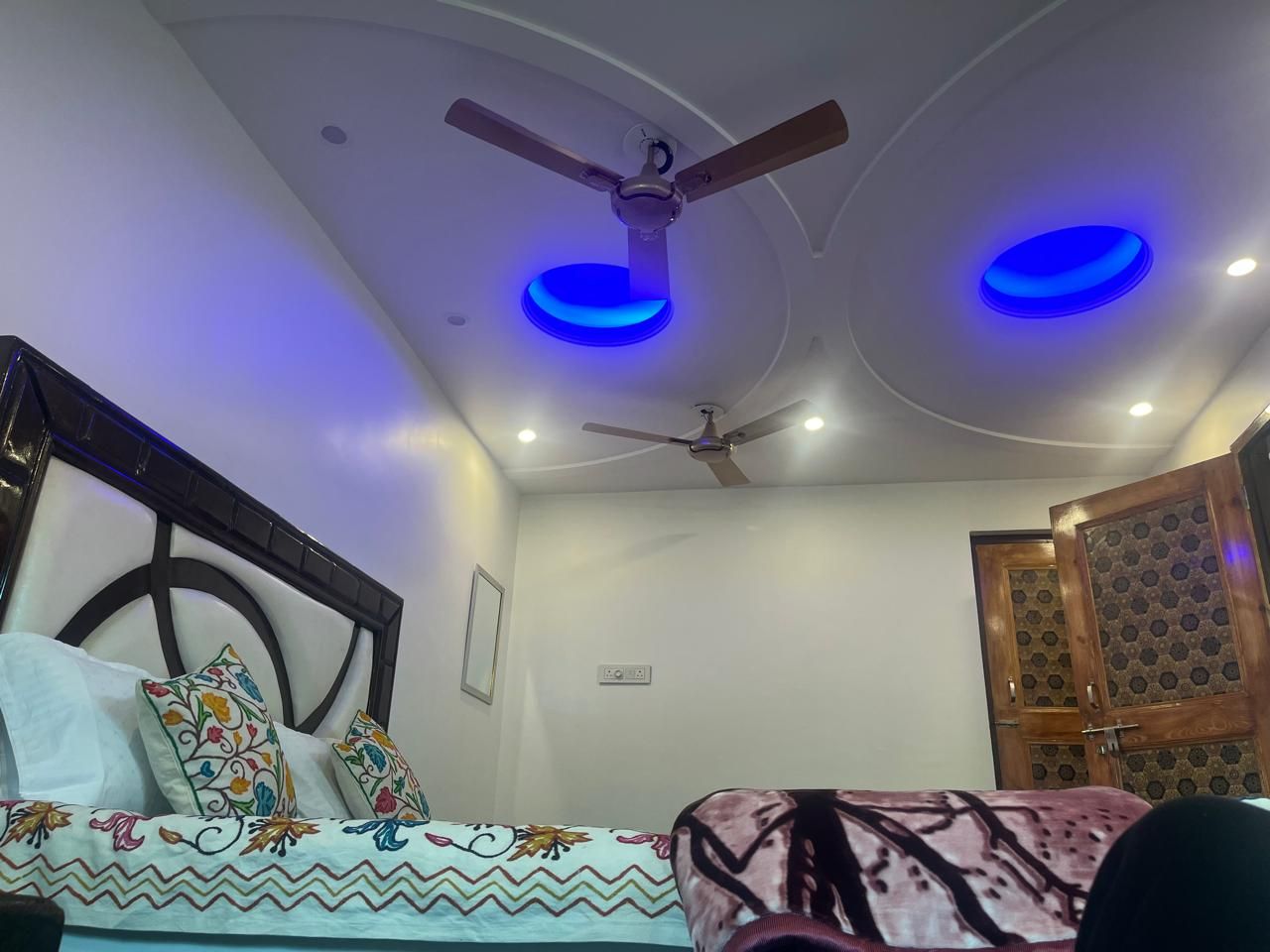 Quarto com cama, ventilador de teto e duas luzes azuis no teto.