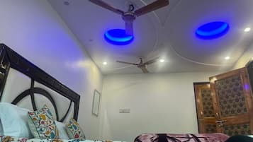 Quarto com cama, ventilador de teto e duas luzes azuis no teto.