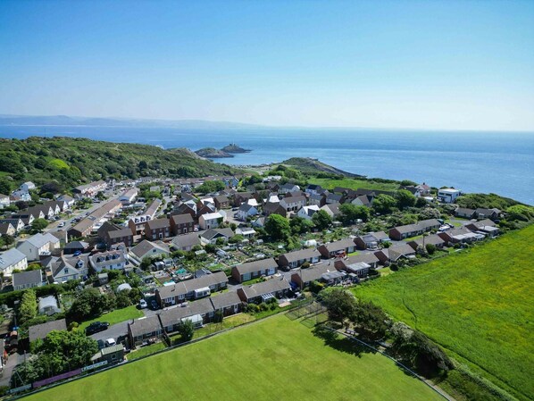 A coastal residential area with houses, a clear view of the sea, and a hilly landscape in the background. - Cosy Cottage - 2 Bedroom Cottage - Mumbles (Swansea)