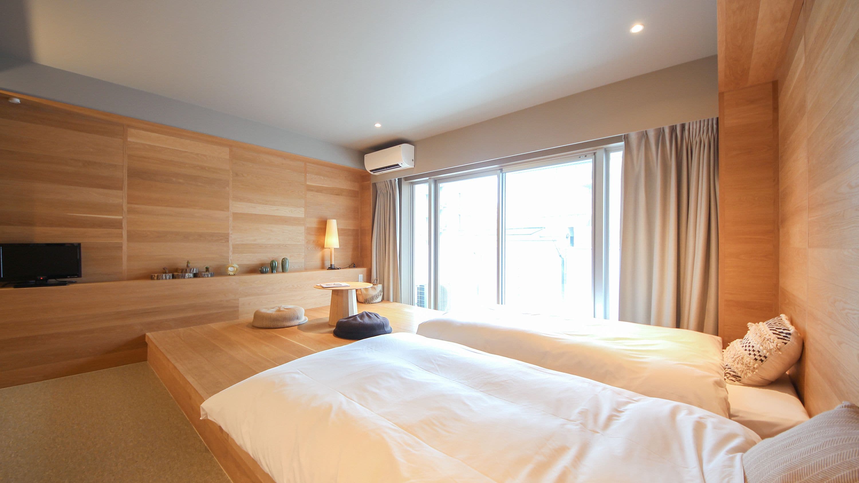 A modern hotel room with a large bed, a flat-screen TV, a bedside table, and a window with curtains.