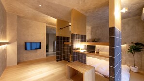A modern bathroom with a wooden bench, a flat-screen TV mounted on the wall, and a small table with a laptop and cup.