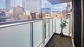 Un balcon agrémenté d’un pot de fleurs, doté d’une rambarde en verre et offrant une vue sur le paysage urbain.