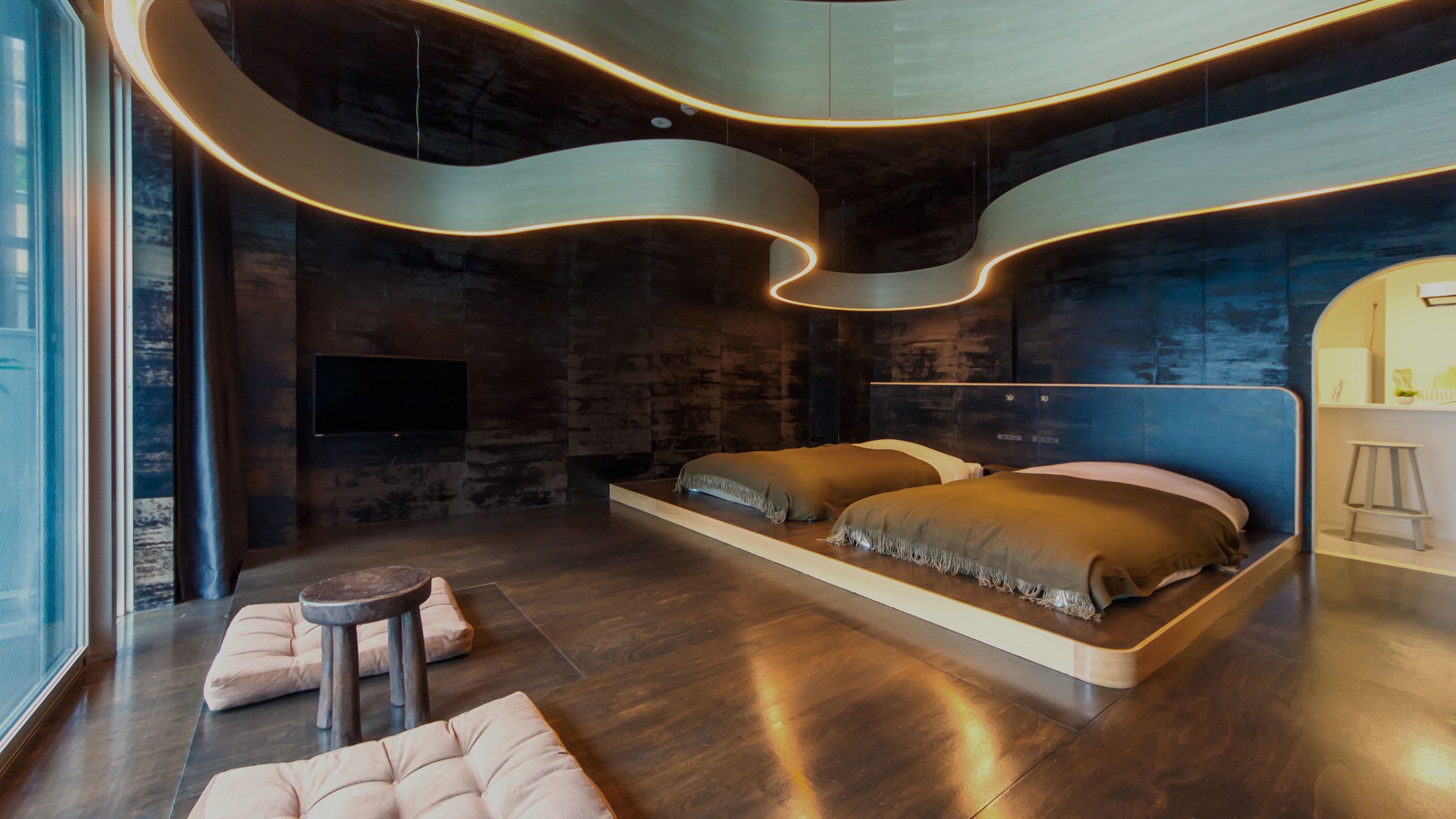 A modern bedroom with a curved ceiling, a large bed, a TV, and a seating area.