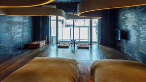Un interior modern amb un terra de fusta, dues zones d'seure amb coixins, una taula petita i una finestra gran que ofereix vistes cap a l'exterior.