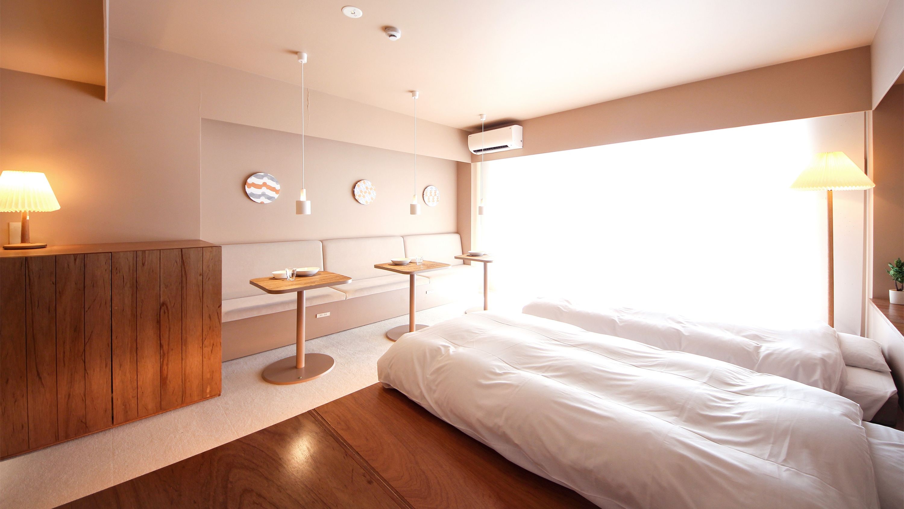 A modern hotel room with a large bed, a wooden cabinet, a small table with a bowl, and a wall-mounted air conditioning unit.