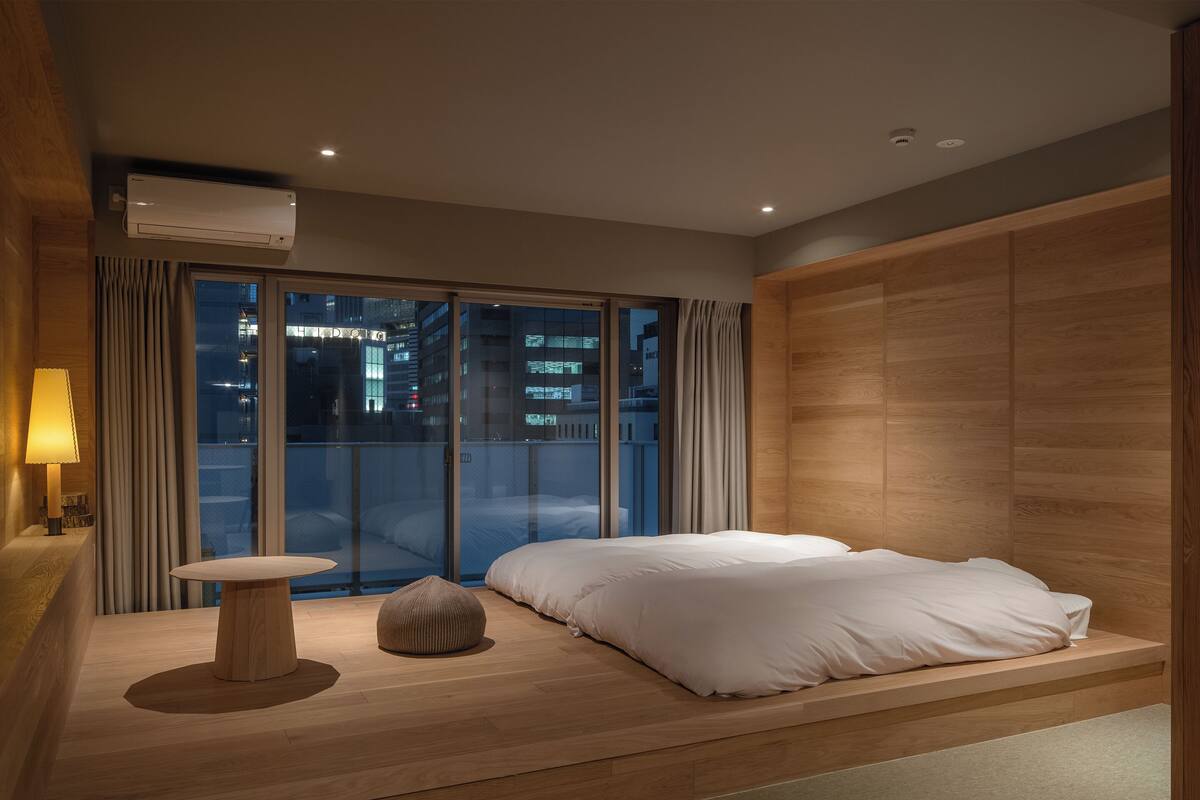 A modern bedroom with a bed, a bedside table, and a view of the city at night.
