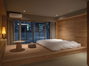 A modern bedroom with a bed, a bedside table, and a view of the city at night. - SEVENSTORIES (Nagoya)
