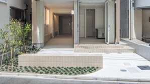 Une entrée moderne avec un passage couvert, un petit espace jardin et une vue dégagée sur l’intérieur du bâtiment.