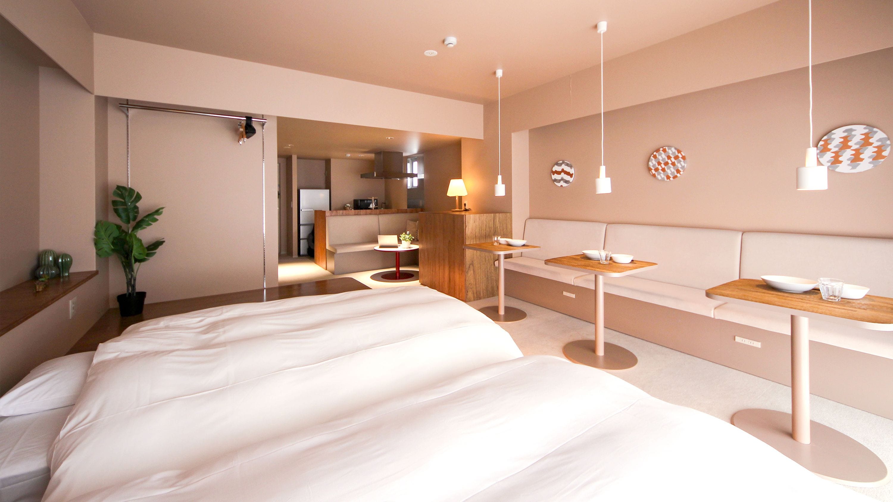 Una habitación de hotel moderna con una cama grande, un área de descanso con una mesa y sillas, una kitchenette pequeña y un baño visible a través de una puerta abierta.