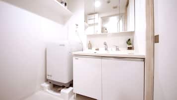 A modern bathroom with a built-in washing machine, a sink with a mirror, and a small potted plant.