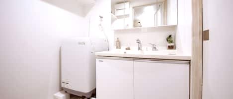 Een moderne badkamer met een ingebouwde wasmachine, een wastafel met spiegel en een kleine potplant.