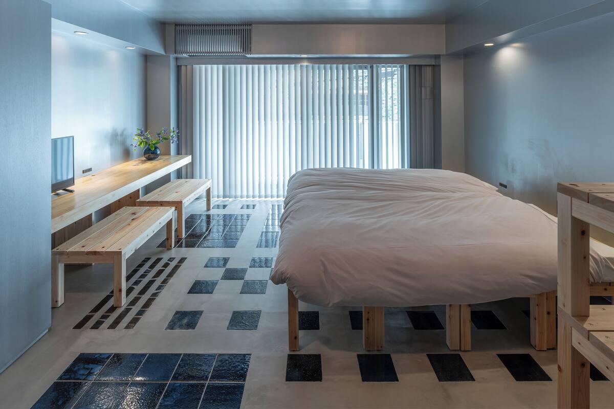 A modern bedroom with a large bed, wooden furniture, a TV, and a view of the outdoors through large windows.