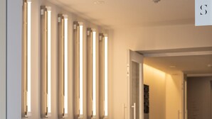 Un couloir doté d’un sol carrelé, d’un banc et d’une série de luminaires verticaux fixés au mur.