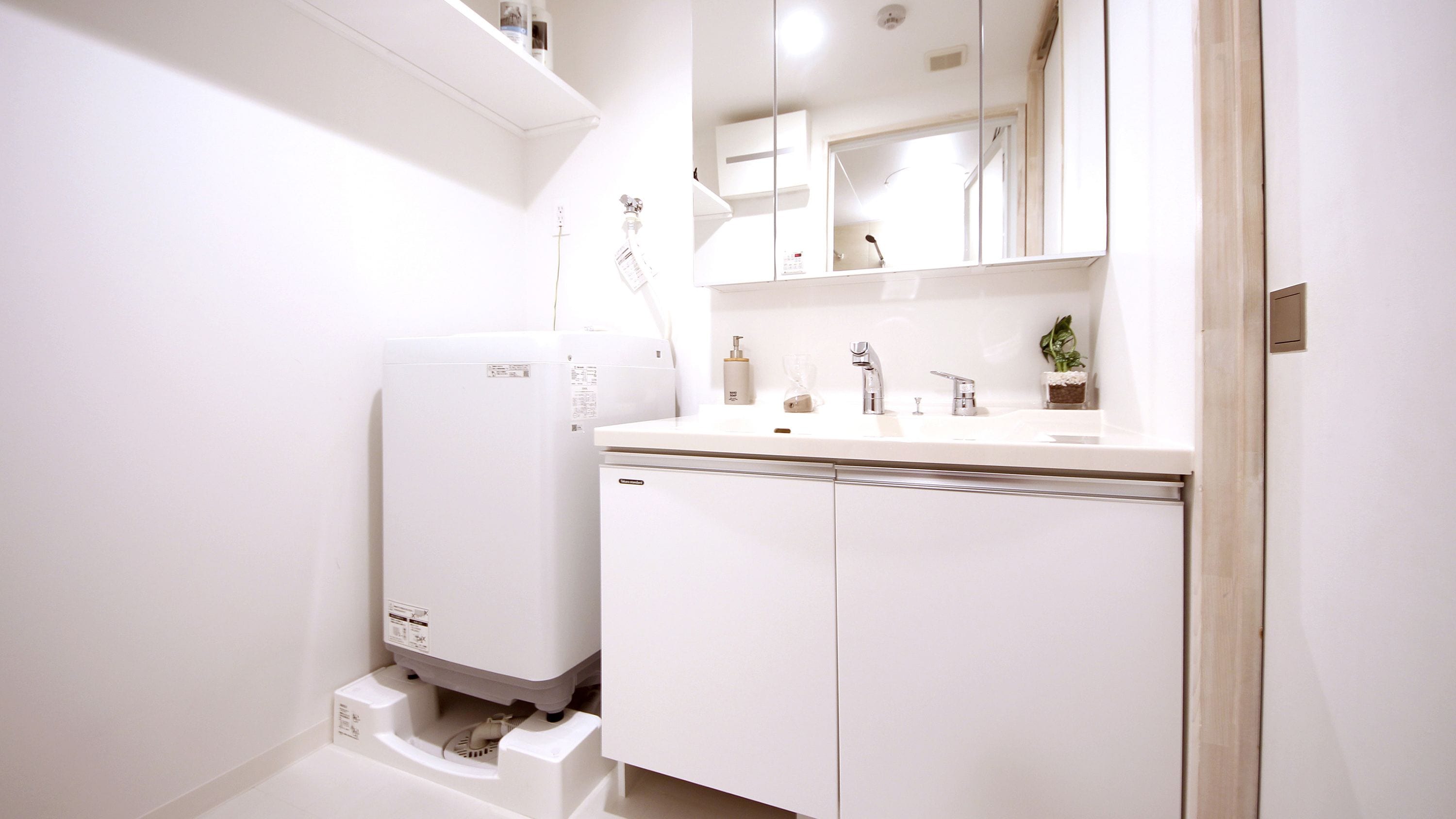 Une salle de bain moderne équipée d’un lave-linge intégré, d’un lavabo avec un miroir et d’une petite plante en pot.