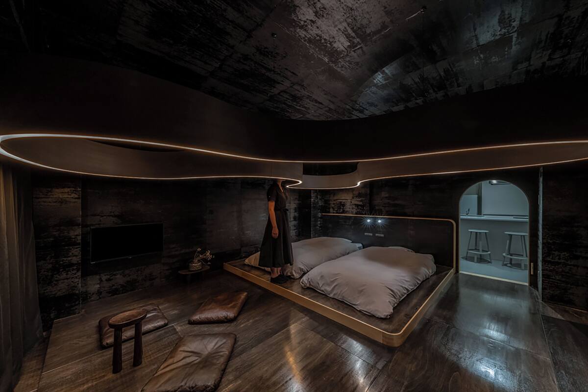 A modern bedroom with a large bed, a small seating area, and a unique ceiling design.