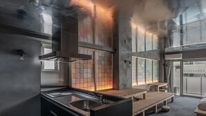 Une cuisine moderne dotée d’un évier en acier inoxydable, d’un banc en bois et offrant une vue sur la ville grâce à de grandes fenêtres.