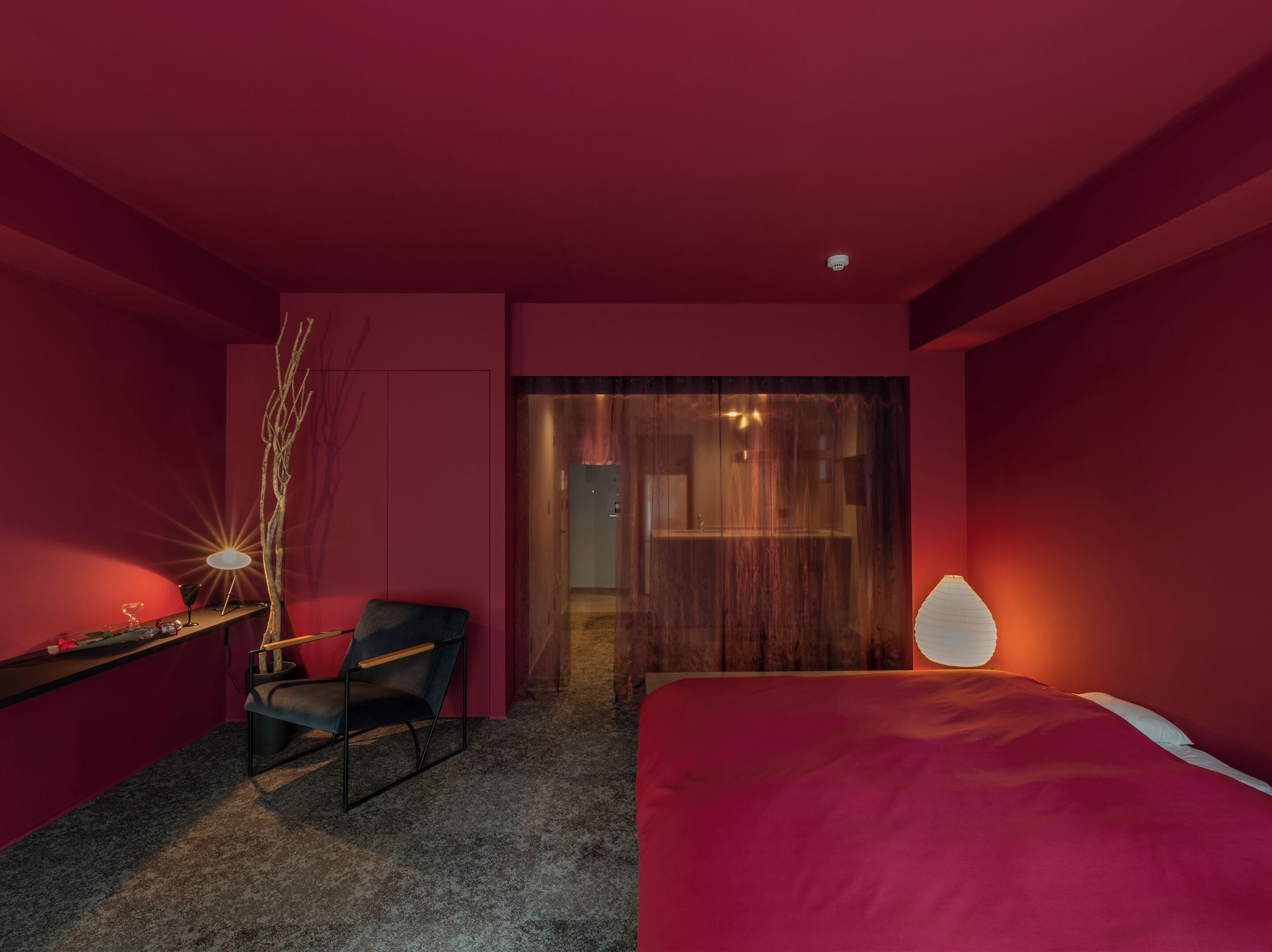 Un dormitorio moderno con temática roja, que incluye una cama, un escritorio, una silla y una lámpara.