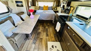 A compact RV interior with a kitchenette, a dining area, and a sleeping berth.
