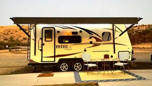 A recreational vehicle with a covered dining area, a small table, and two chairs.