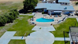 An aerial view of a property with a swimming pool, a covered patio area, and a large lawn.