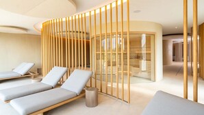 A modern spa with three lounge chairs, a wooden partition, and a glass-walled treatment room.