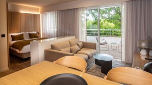 A modern hotel room with a bed, a sofa, a dining table, and a balcony with outdoor seating. - Horizon Resort Massane by Interhome (Baillargues)