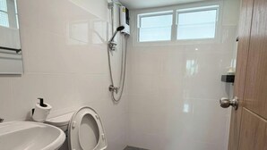 A small, clean bathroom with a toilet, sink, and shower. - NamasStay Silom (Bangkok)