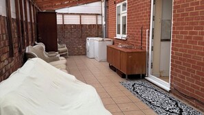 A small, enclosed room with a wooden ceiling, a brick wall, a washing machine, a wooden cabinet, and a bed. - 2 bed-Sleeps 4-Private Patio-Pets-Near Heathrow (Hounslow)