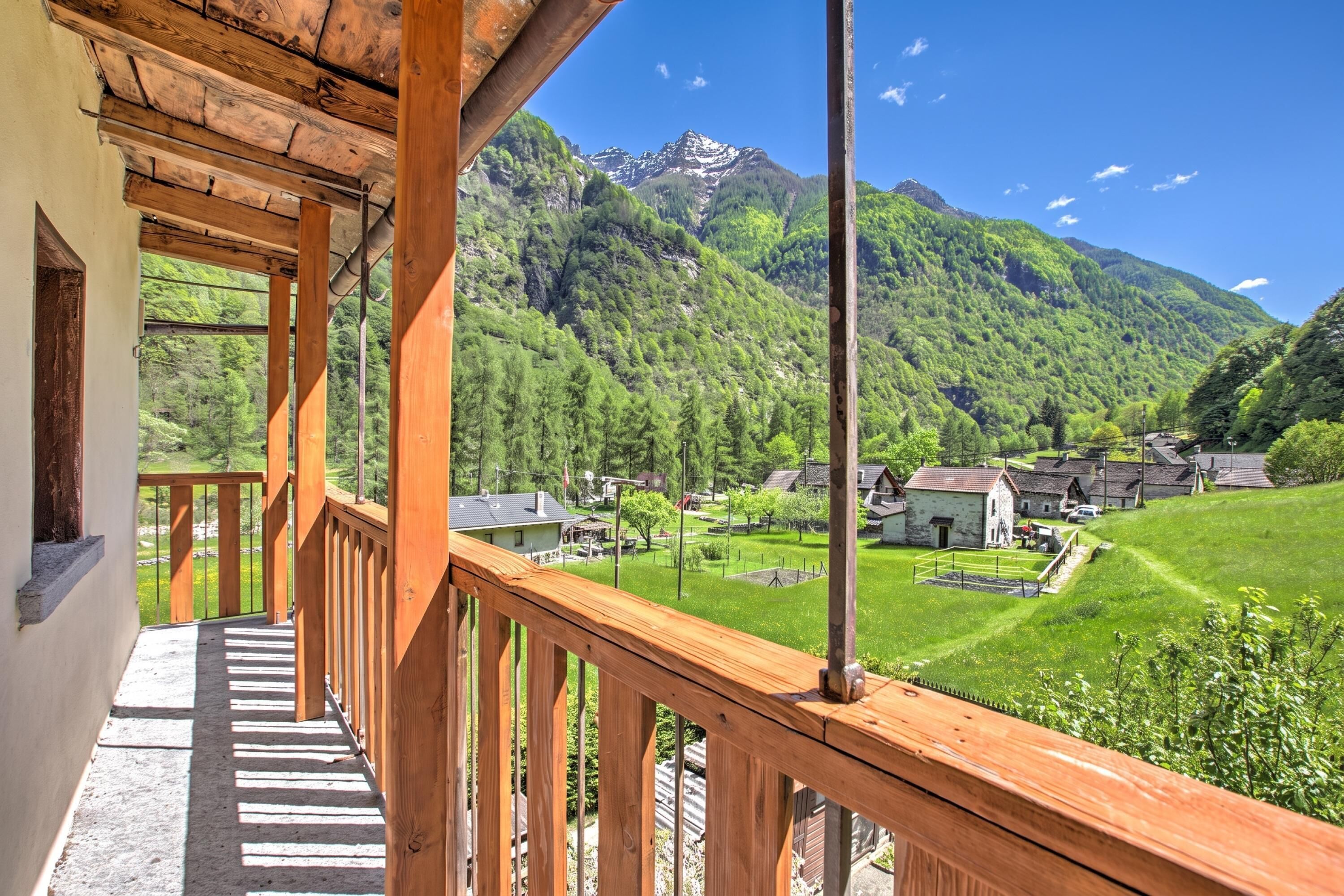 A balcony with a wooden railing overlooking a mountainous landscape with a village below.