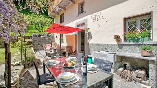 Ulkoterassi, jossa on pöytä kahdelle, punainen aurinkovarjo ja kiviseinä.