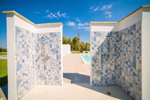 A modern outdoor shower area with geometric patterned tiles, a pool, and a clear sky.