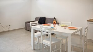 Un comedor con una mesa y sillas blancas, un sofá y una botella de vino.