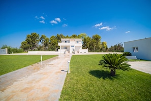 Uma casa moderna de dois andares, com entrada central, cercada por gramados bem cuidados e árvores.