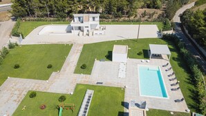 Una casa moderna de dos pisos con piscina, un patio con sillones de descanso y un pequeño parque infantil.